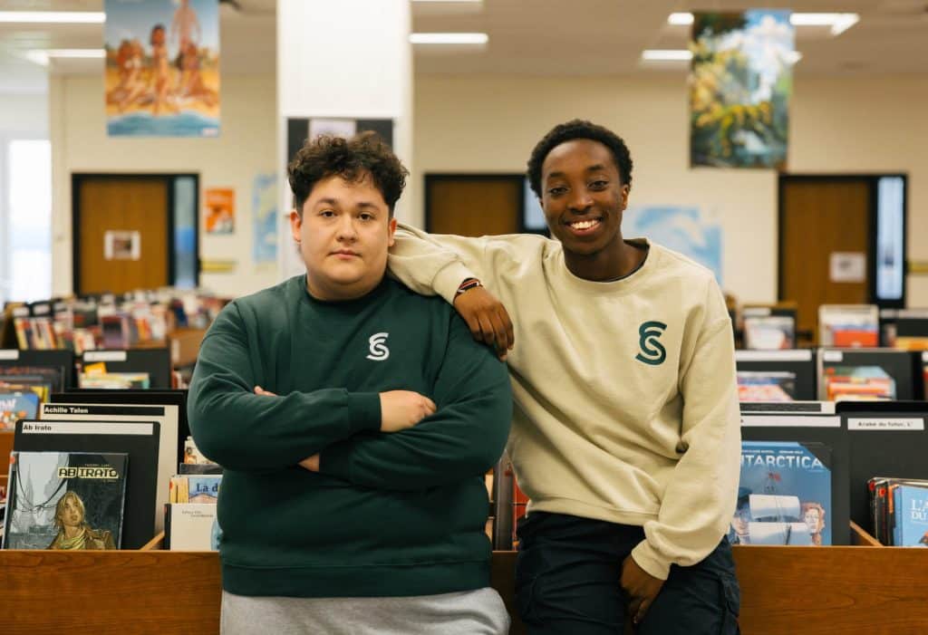 Deux étudiants masculins regardent la caméra debout dans la bibliothèque