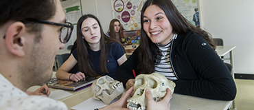 une jeune fille souriante en avant-plan avec d'autres jeunes qui découvrent des crânes de la préhistoire