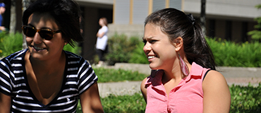 Jeune fille et une femme adulte sont assises sur la pelouse et sourient.
